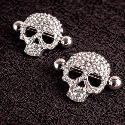 Pair of skull-shaped nipple shields with rhinestones on a dark textured background