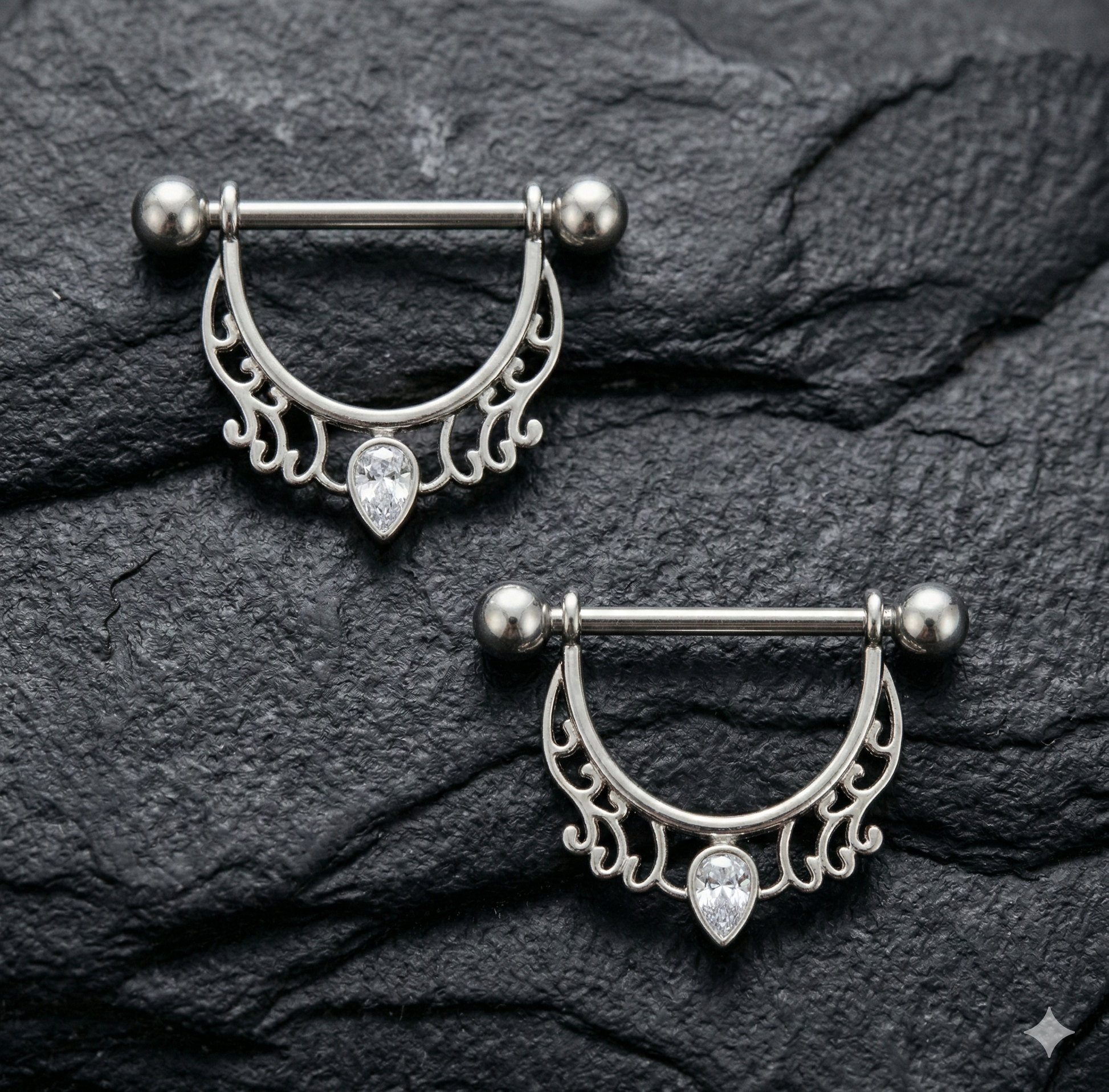 Pair silver nipple rings with intricate designs on a dark stone surface