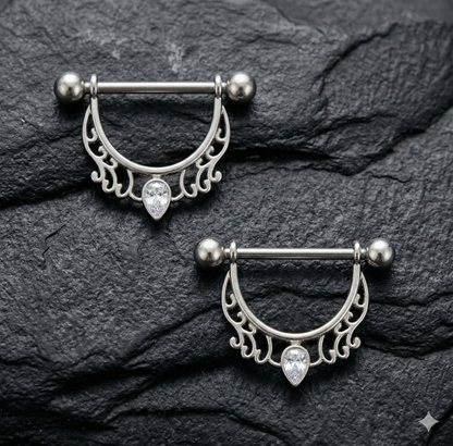 Pair silver nipple rings with intricate designs on a dark stone surface
