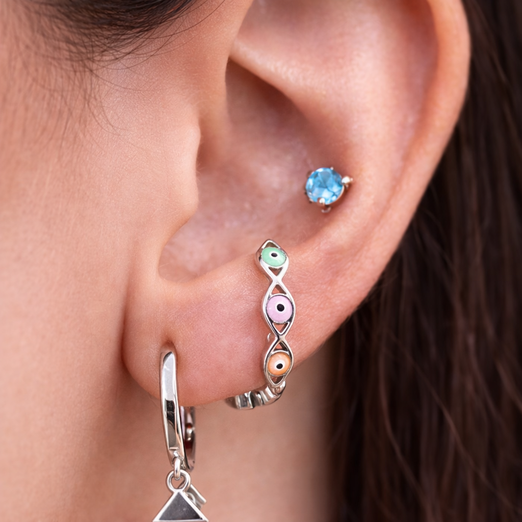 Close-up of an ear wearing a silver hoop earring with a triangle charm and a colorful gemstone earring.