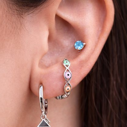 Close-up of an ear wearing a silver hoop earring with a triangle charm and a colorful gemstone earring.