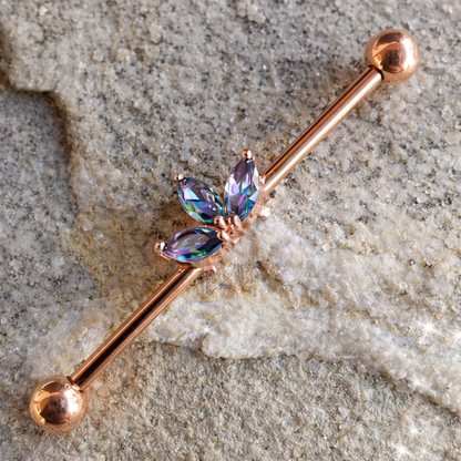 Rose gold barbell with multicolored gemstones on a textured stone surface