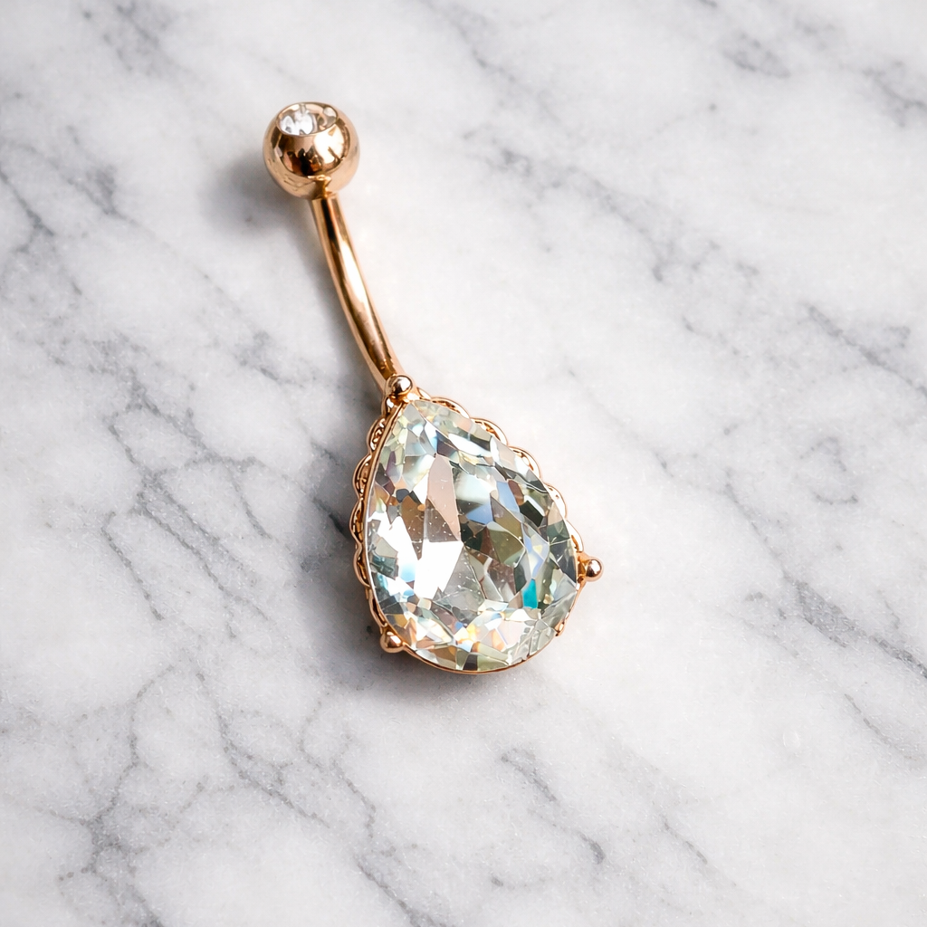 Rose gold belly button ring with a large clear gemstone on a marble background