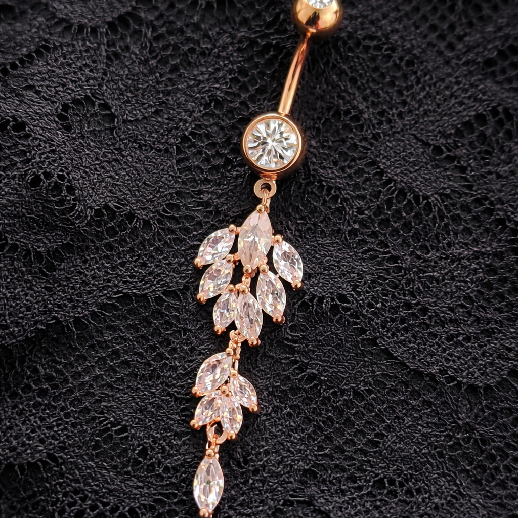 Rose gold belly button ring with leaf-shaped gemstones on a black textured background