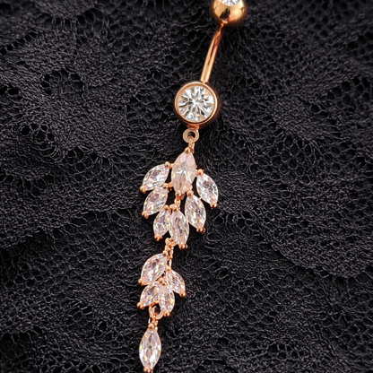 Rose gold belly button ring with leaf-shaped gemstones on a black textured background