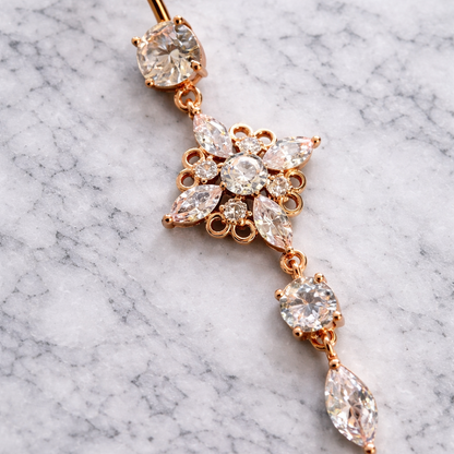 Rose gold belly button ring with clear gemstones on a marble background