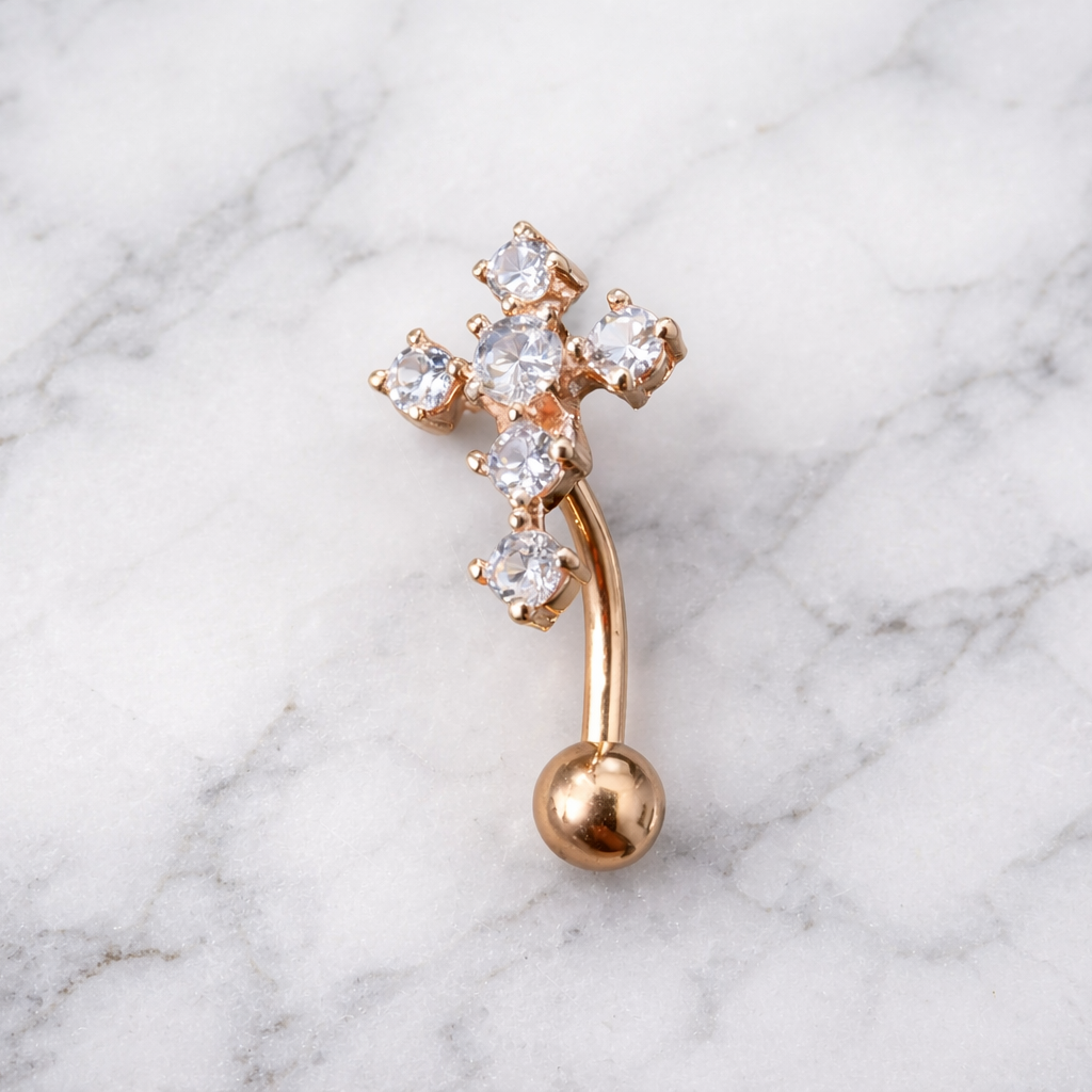 Rose gold cross navel ring with clear gemstones on a marble background