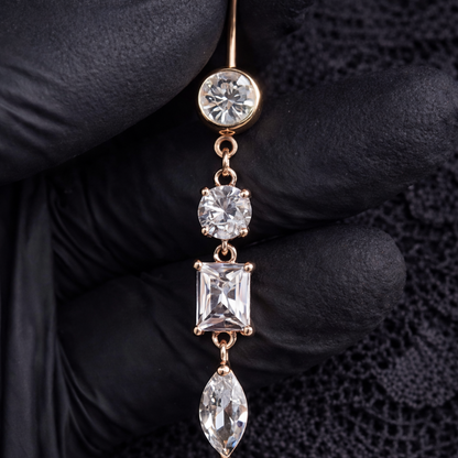 Rose Gold belly ring with clear gemstones held by a gloved hand on a dark background
