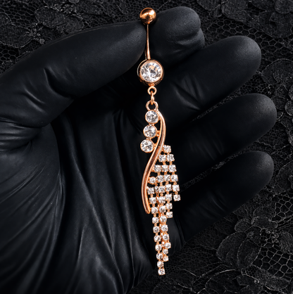 Rose gold navel bar with clear stones held by a gloved hand on a black lace background