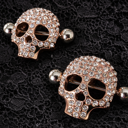 Rose gold skull nipple shields with clear gemstones on a black textured background