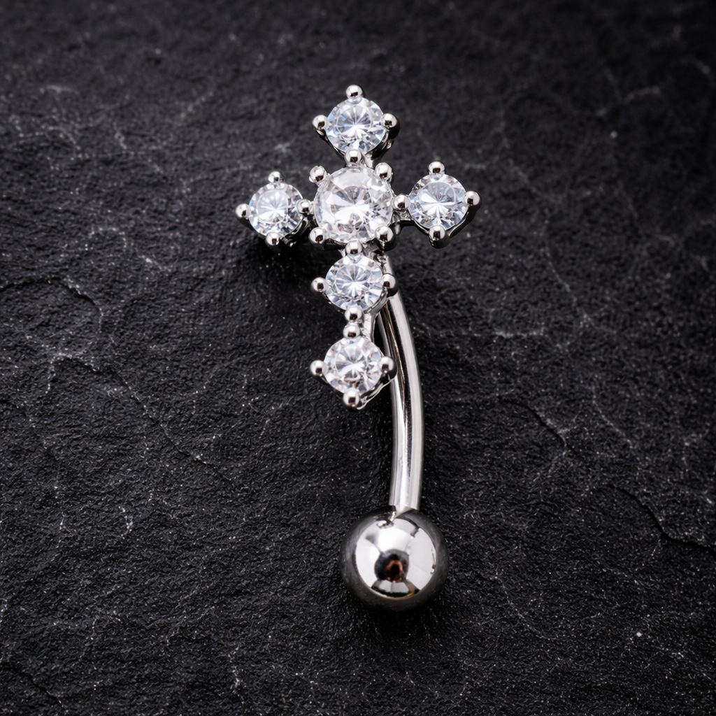 Silver cross-shaped belly button ring with clear gemstones on a black textured background