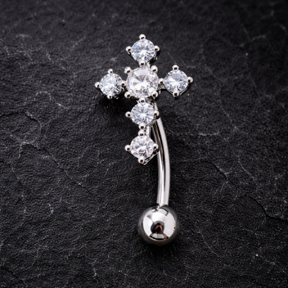 Silver cross-shaped belly button ring with clear gemstones on a black textured background