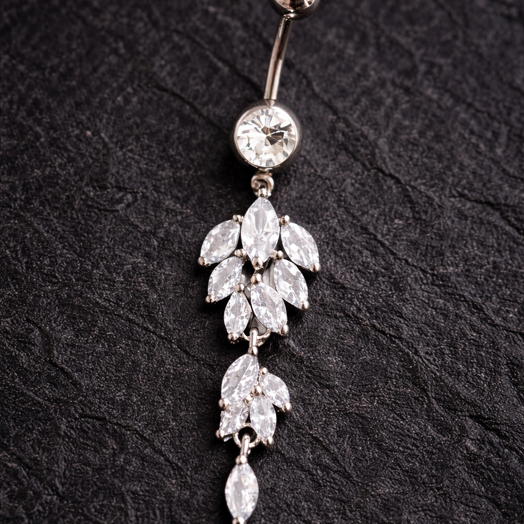 Decorative belly button ring with leaf-shaped crystals on a black textured background