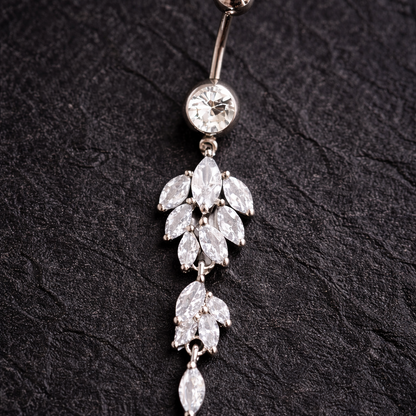 Decorative belly button ring with leaf-shaped crystals on a black textured background