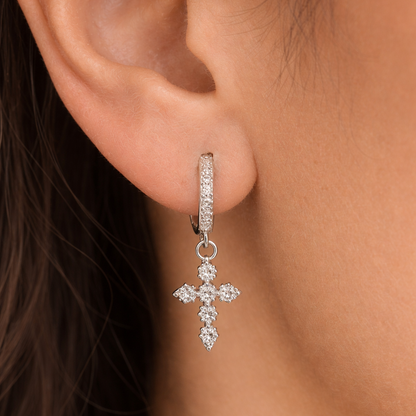 Close-up of a person wearing a silver hoop earring with a cross pendant.
