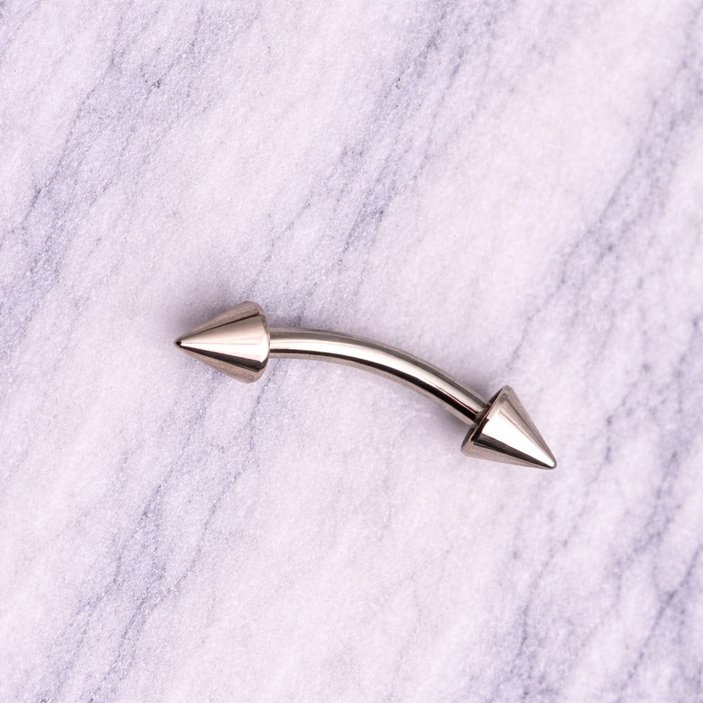 Silver-colored curved spike eyebrow/rook bar on a marble background