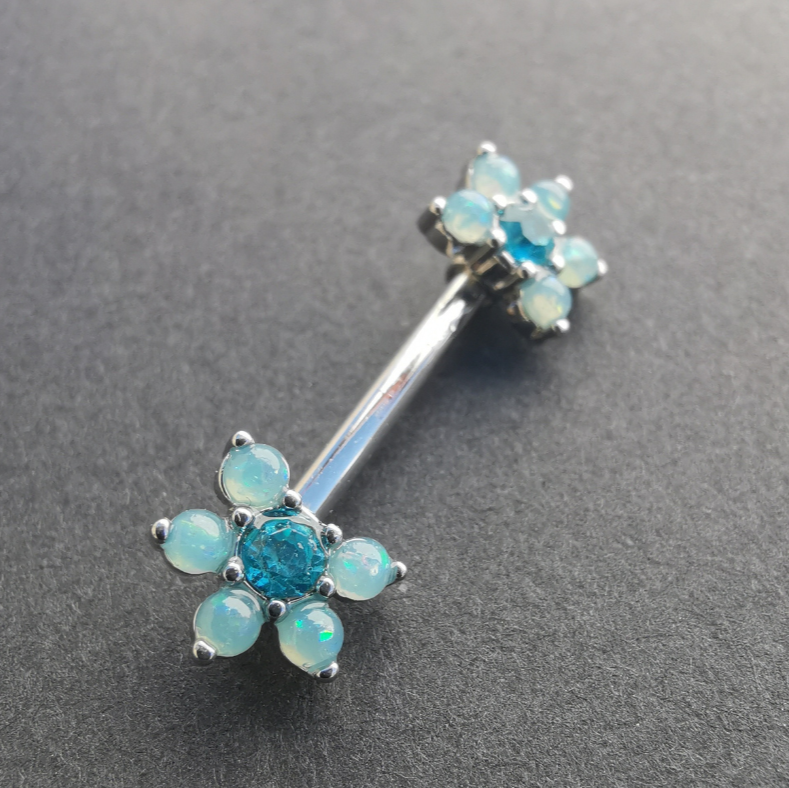 Stylish floral nipple piercing with a blue pearl center, CZ stones, and a 14G silver surgical steel barbell.