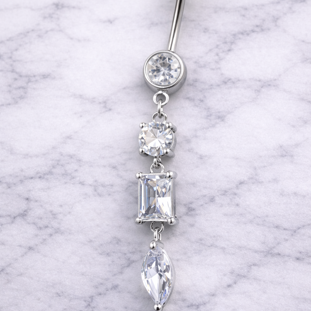 Silver belly button ring with clear gemstones on a marble background