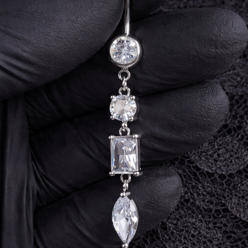 Silver belly button ring with gemstones held by a gloved hand on a black lace background