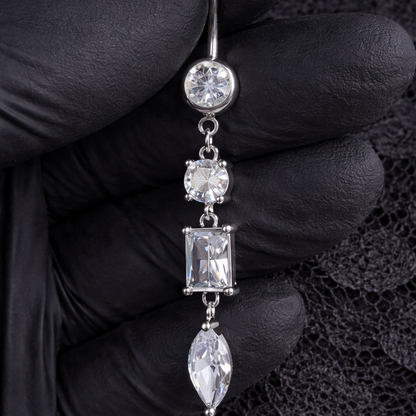 Silver belly button ring with gemstones held by a gloved hand on a black lace background