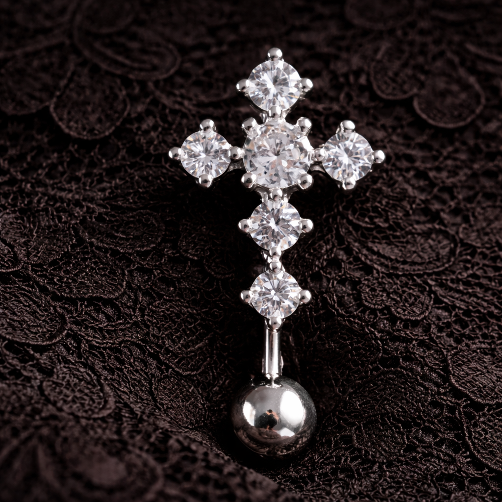 Silver cross-shaped belly ring with clear gemstones on a dark textured background