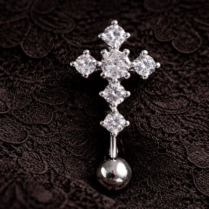 Silver cross-shaped belly ring with clear gemstones on a dark textured background
