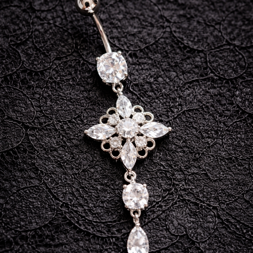 Silver belly button ring with floral design on a black textured background