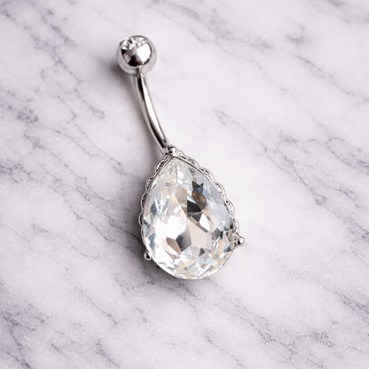 Belly button ring with a large teardrop-shaped gemstone on a marble background