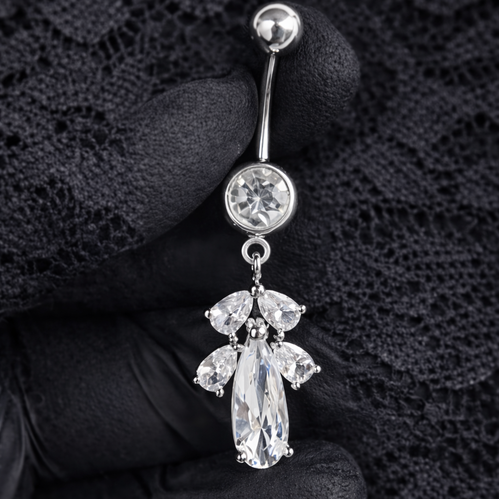 Silver belly button ring with gemstones held by a gloved hand on a black lace background