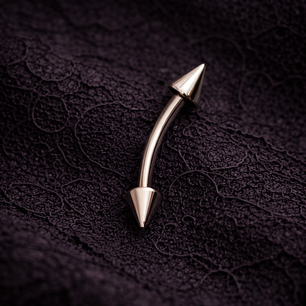 Silver colored metallic spiral eyebrow/rook bar with pointed ends on a textured dark ba