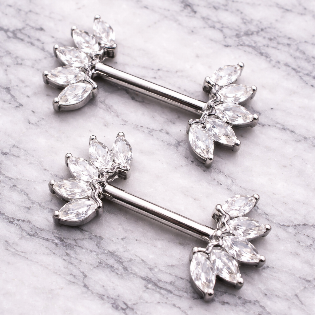 Silver crown nipple bars with clear gemstones on a marble background
