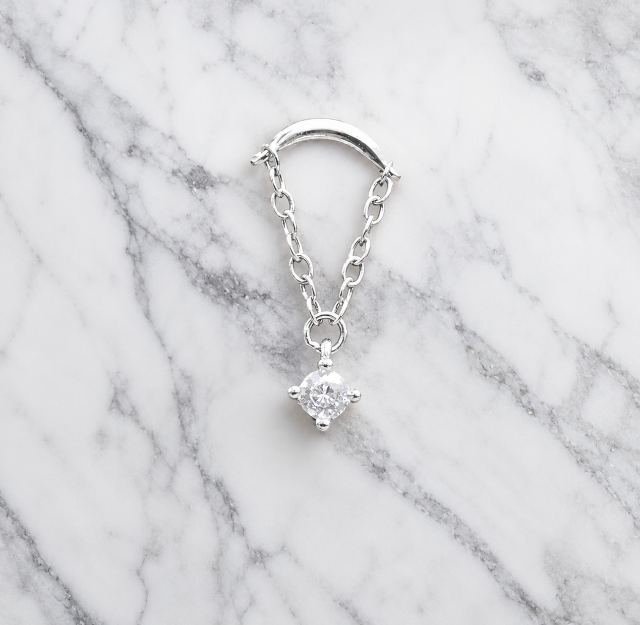Silver earring with a clear gemstone on a marble background