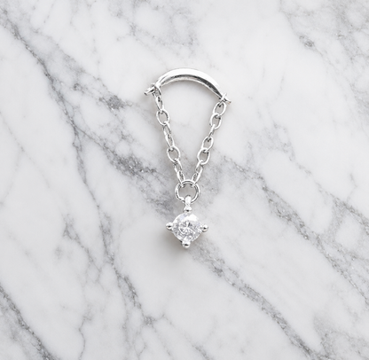 Silver earring with a clear gemstone on a marble background
