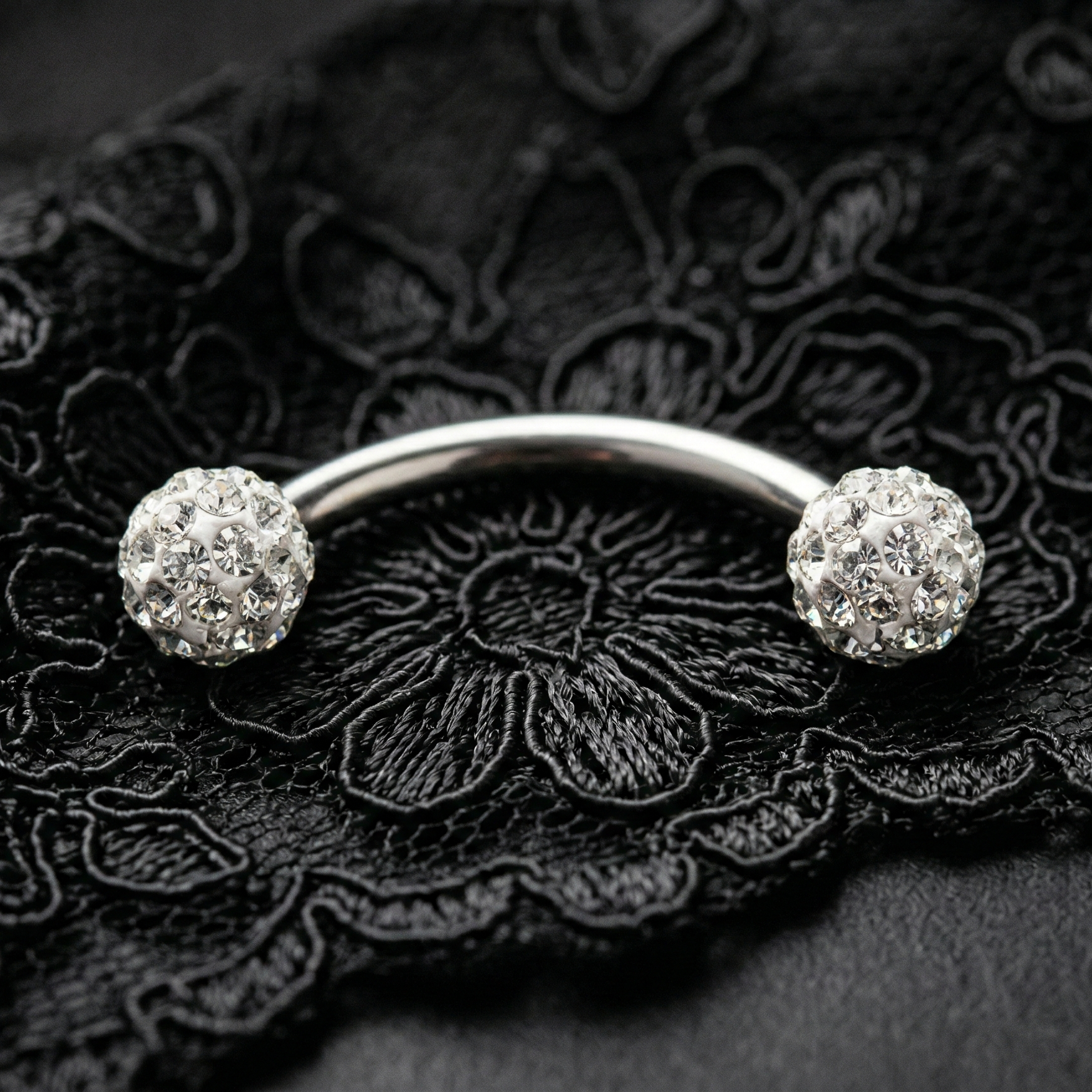 Silver eyebrow bar with two round gemstones on a black lace background