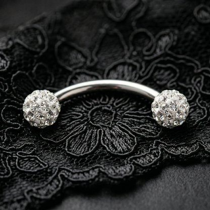 Silver eyebrow bar with two round gemstones on a black lace background