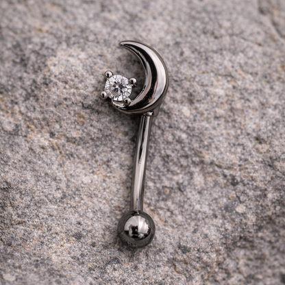 Silver eyebrow/rook bar with a moon and star design on a stone surface