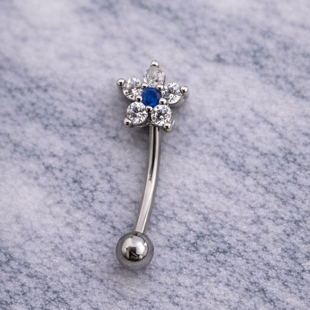Silver eyebrow/rook bar with blue gemstone on a marble background