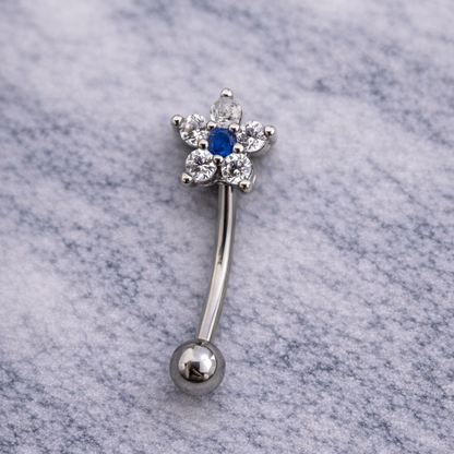 Silver eyebrow/rook bar with blue gemstone on a marble background