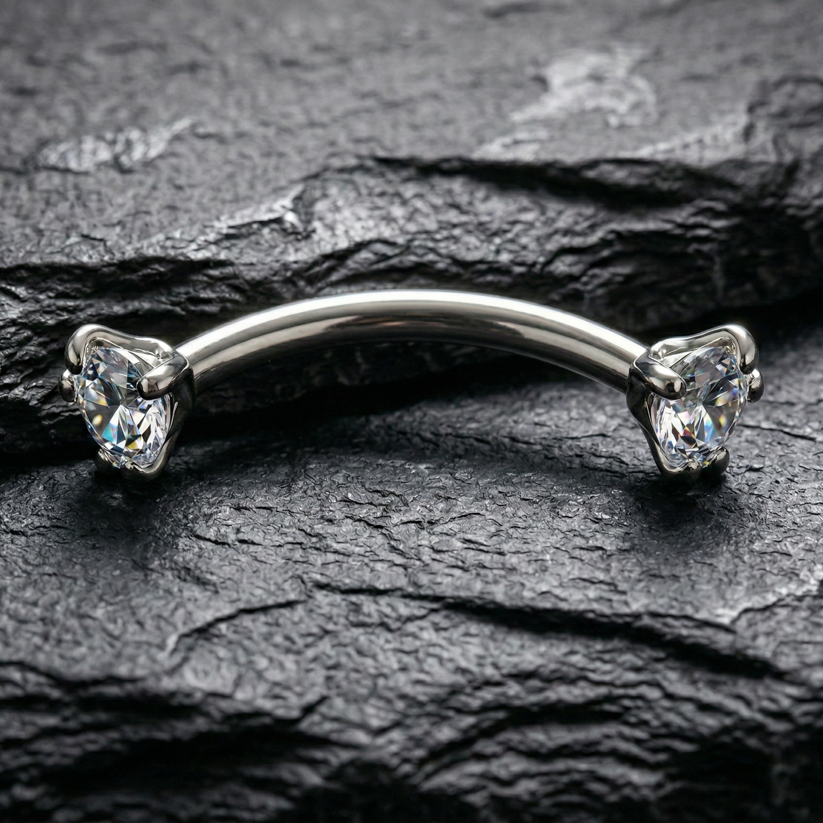 Silver eyebrow/rook bar with clear gemstones on a dark stone surface