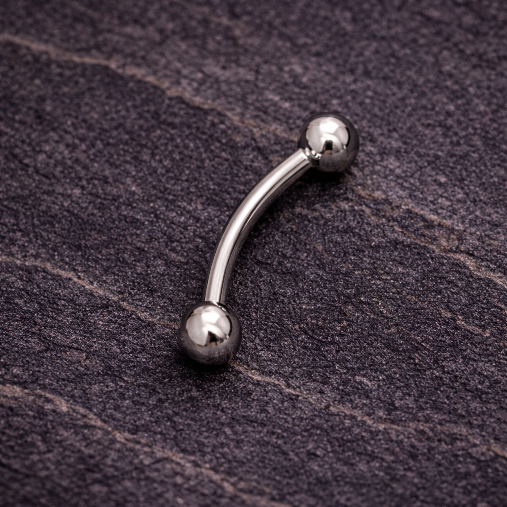 Silver eyebrow/rook curved barbell on a textured dark surface