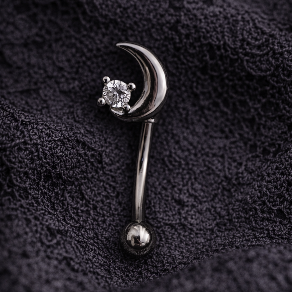 Silver eyebrow/rook earring shaped like a crescent moon with a diamond on a black textured background