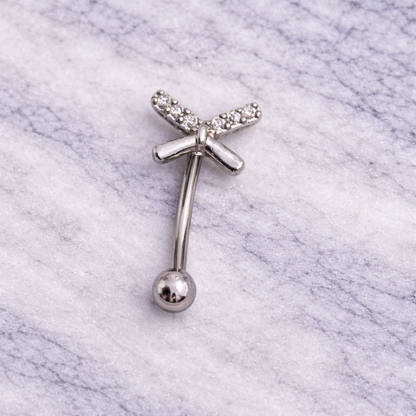 Silver eyebrow/rook piercing bar with a bow design on a marble background
