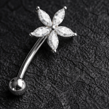 Silver eyebrow/rook piercing bar with a floral design on a dark textured background