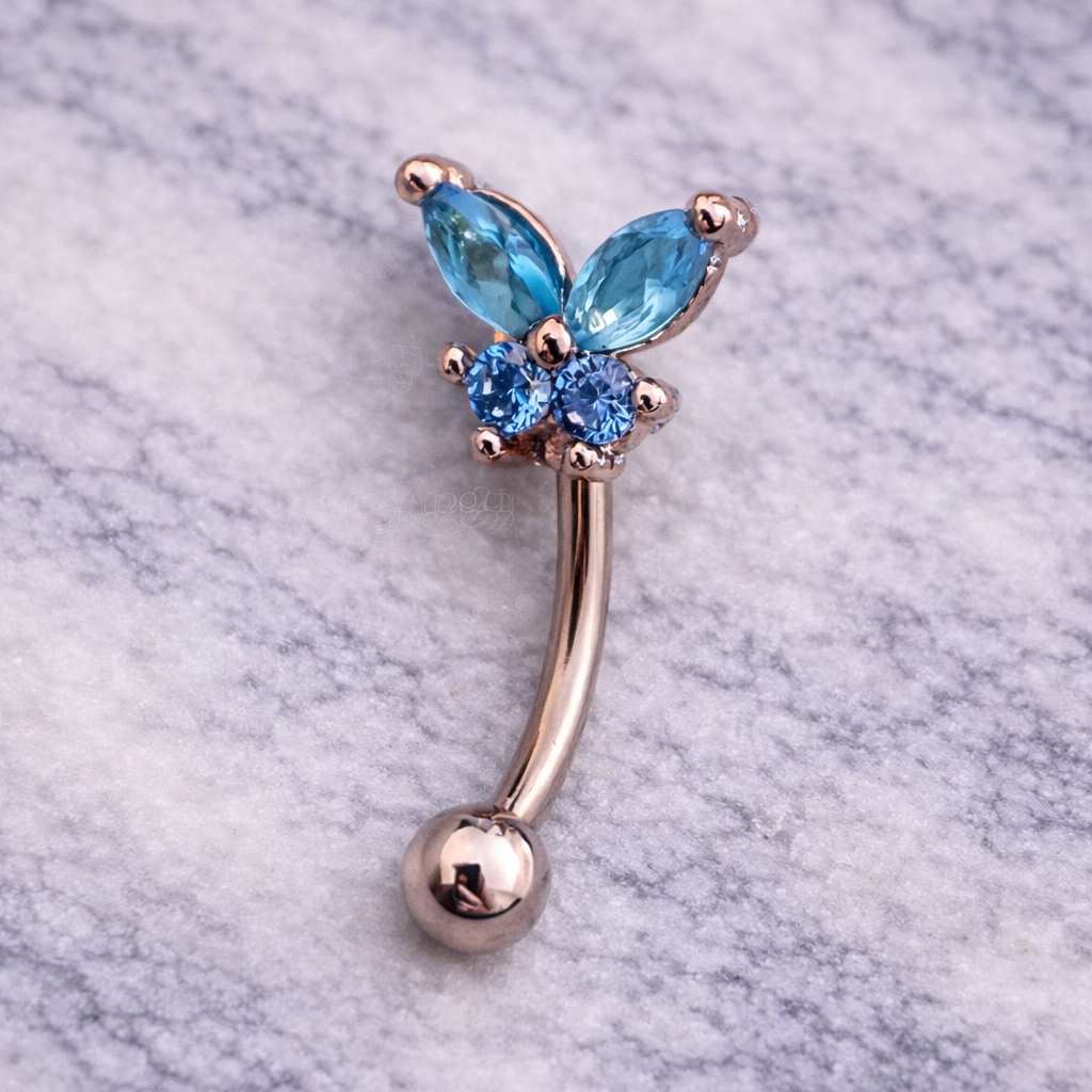 Silver eyebrow/rook piercing barbell with blue gemstones on a marble background
