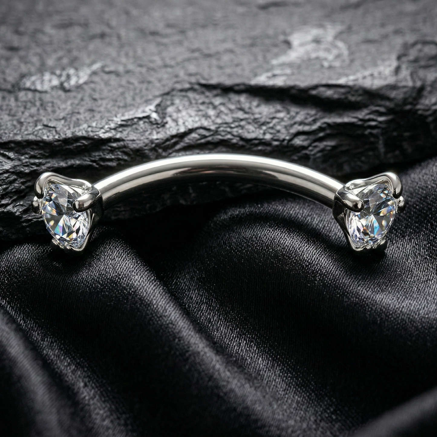 Silver eyebrow/rook piercing barbell with gemstones on a black satin background