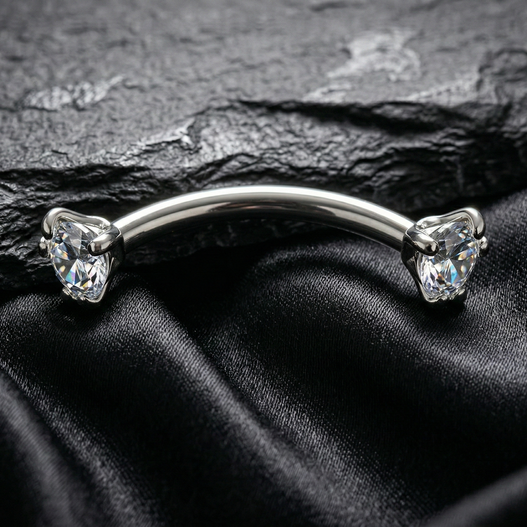 Silver eyebrow/rook piercing barbell with gemstones on a black satin background