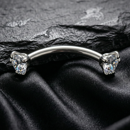 Silver eyebrow/rook piercing barbell with gemstones on a black satin background
