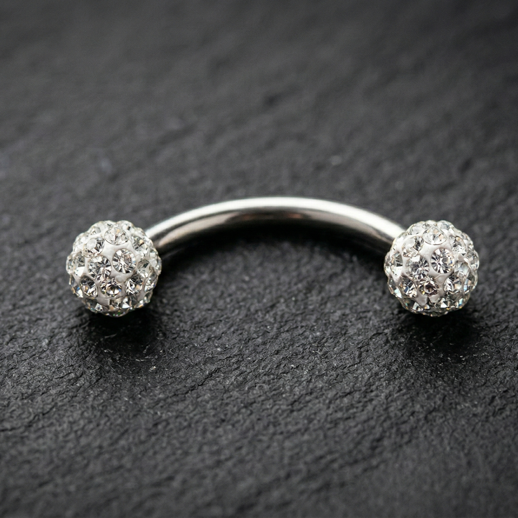Silver eyebrow/rook piercing barbell with spherical ends on a dark surface