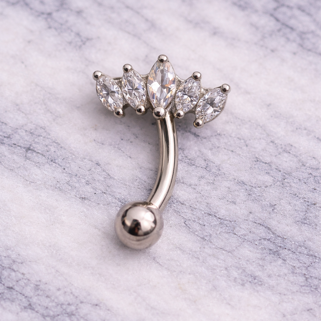 Silver eyebrow/rook ring with clear gemstones on a marble background