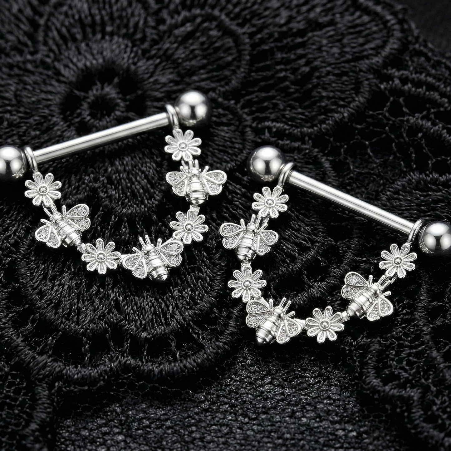 Silver floral nipple bars with bees charms on a black lace background
